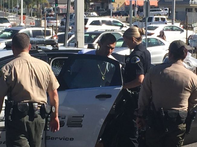 身著白衣的西語裔男性嫌犯中午12時半左右被警方逮捕,押入警車內。(記者高梓原/攝影)