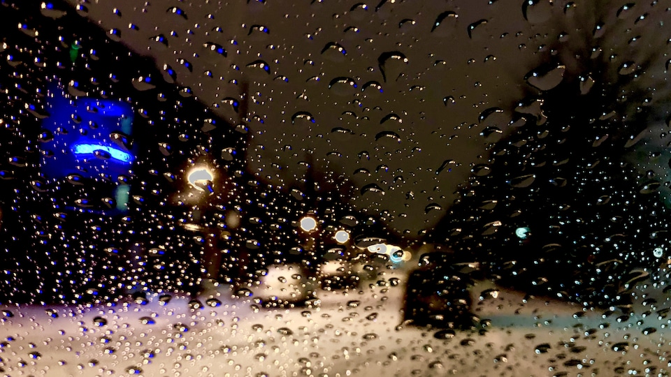 Une vitre recouverte de gouttes d'eau. Hors-champ, une rue enneigÃ©e. 