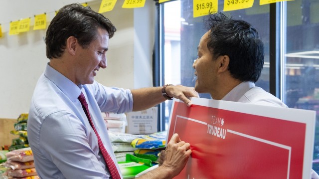 Justin Trudeau signe la pancarte électorale qu'un homme tient dans ses mains.