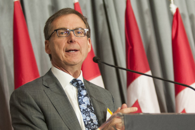 Tiff Macklem speaks at a lecturn with Canadian flags in the background